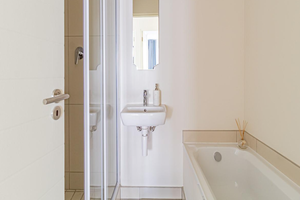 A clean, functional bathroom featuring a white bathtub, a wall-mounted basin, and a separate glass-enclosed shower stall.