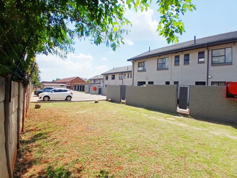 Rear view of the townhouse complex featuring a private garden area, brick boundary walls with electric fencing, and access to the paved driveway.