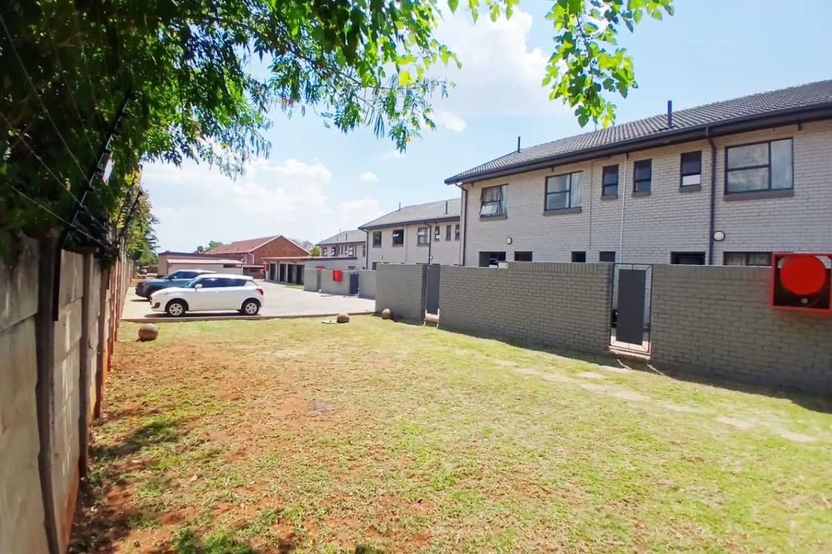 Rear view of the townhouse complex featuring a private garden area, brick boundary walls with electric fencing, and access to the paved driveway.