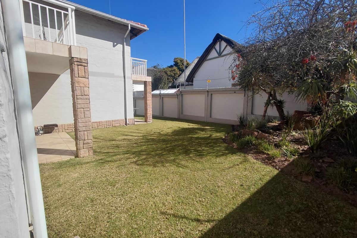 A well-maintained rear garden featuring a tiled patio, stone-clad pillars, and secure perimeter walling with electric fencing.