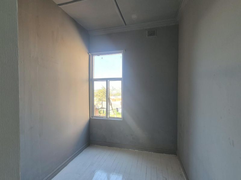 An empty bedroom featuring painted timber flooring, a single casement window, and a ventilation grille, awaiting finishing touches.
