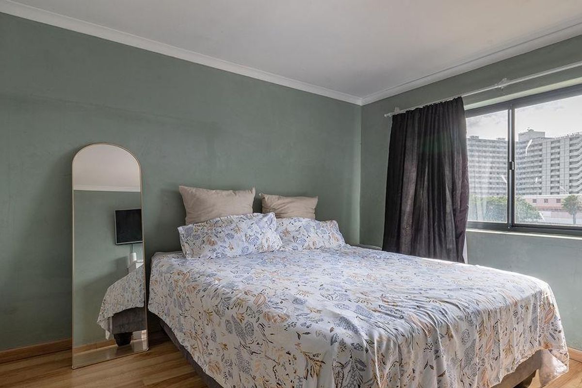 A bedroom featuring light green walls, laminate flooring, and a large window with natural light.