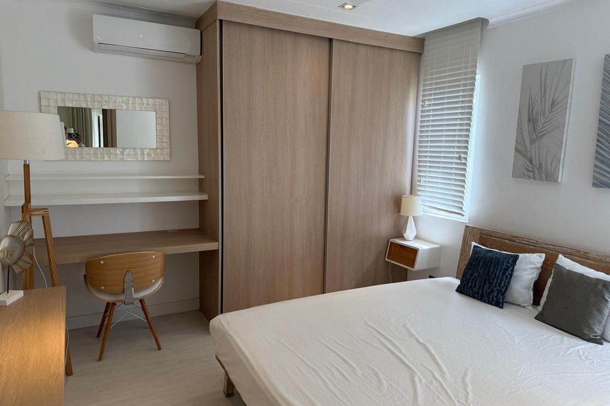 A well-maintained bedroom featuring built-in timber-look sliding wardrobes, a integrated desk workspace, and a wall-mounted split-system air conditioning unit.