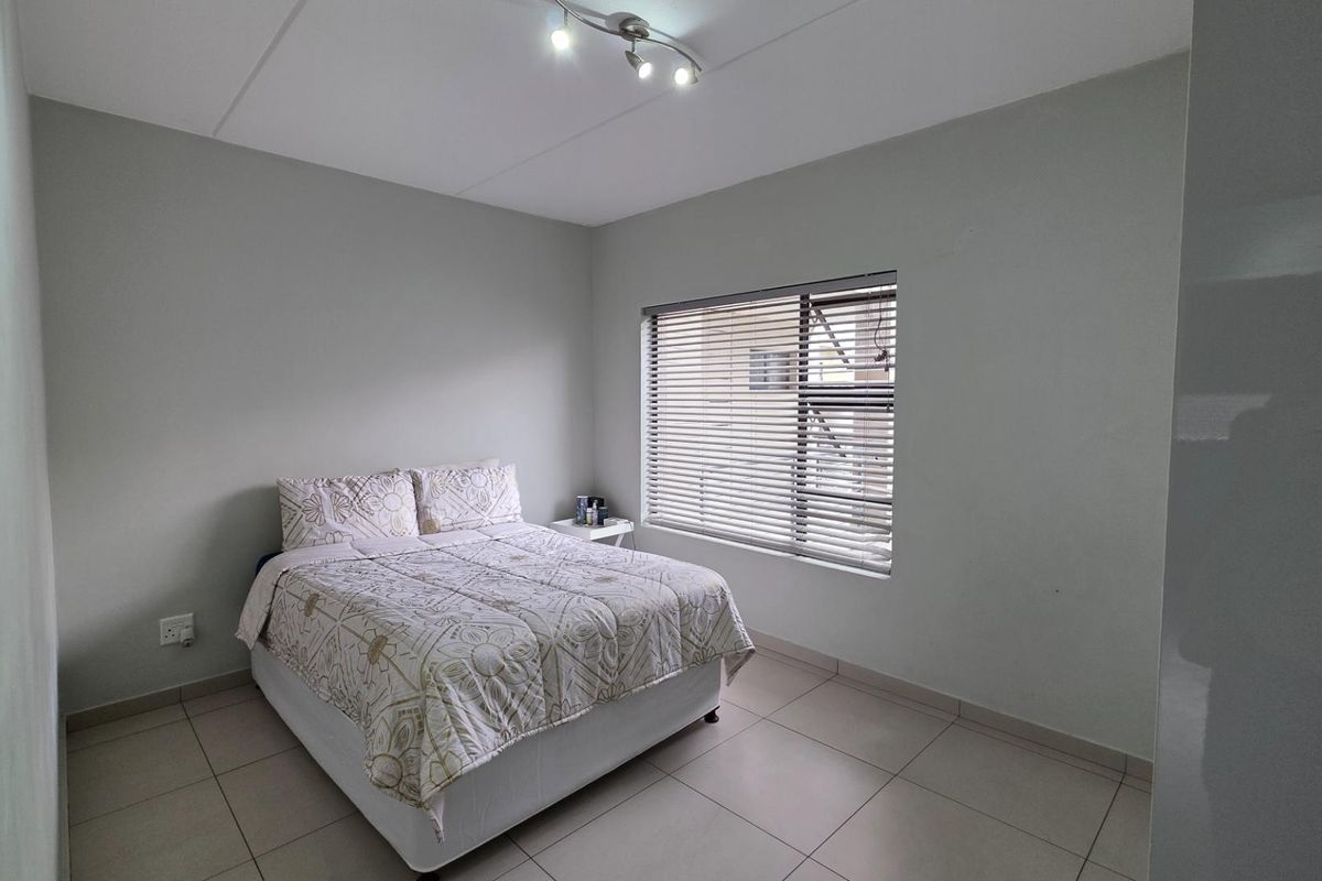 A well-lit bedroom featuring neutral tiled flooring, a window with fitted blinds, and a modern ceiling-mounted light fixture.