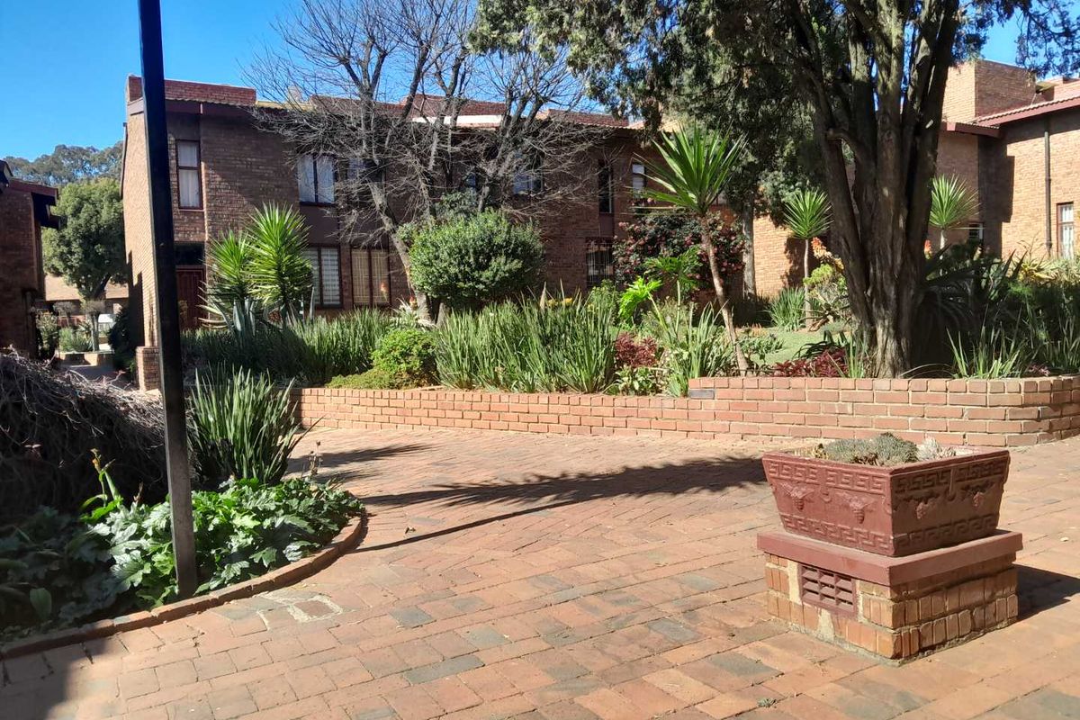 A view of the townhouse complex rear exterior featuring established garden beds, brick paving, and a brick retaining wall.
