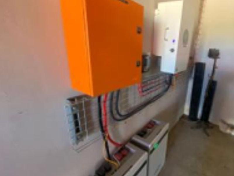 Utility area featuring a wall-mounted solar inverter and lithium battery storage system for off-grid power management.
