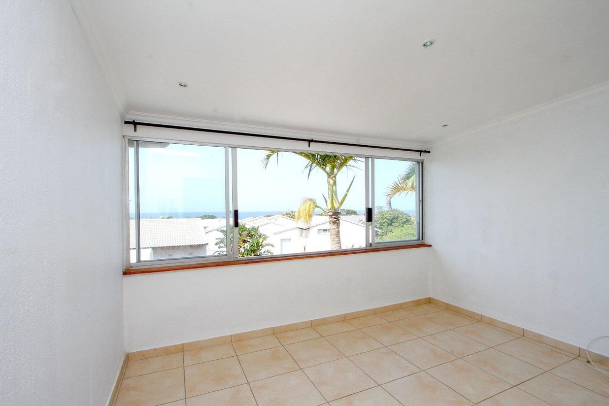 A bright, empty bedroom featuring tiled flooring, recessed downlights, and large aluminium sliding windows offering a pleasant view of the surrounding neighbourhood.