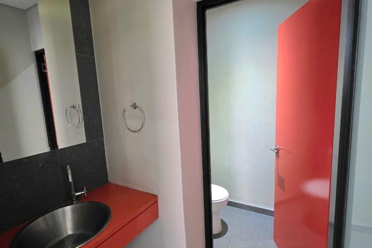 Modern office bathroom featuring a sleek vessel sink, tiled vanity, and a separate toilet cubicle with a bold red door.