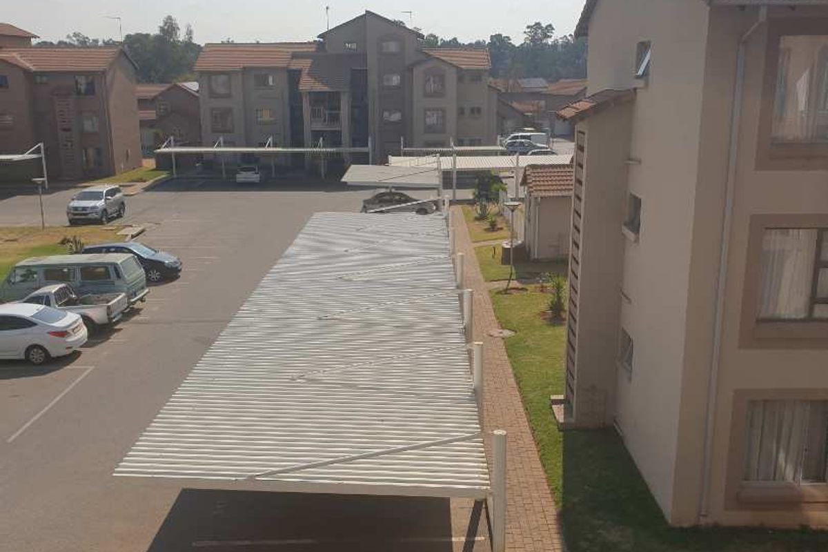 Elevated view of the apartment complex grounds, featuring paved parking areas with covered carports and surrounding landscaped garden spaces.