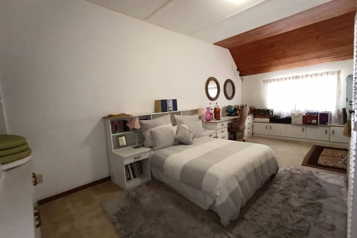 Spacious bedroom featuring a sloped timber ceiling, built-in cabinetry, and a dedicated desk area, offering a functional layout with natural light.