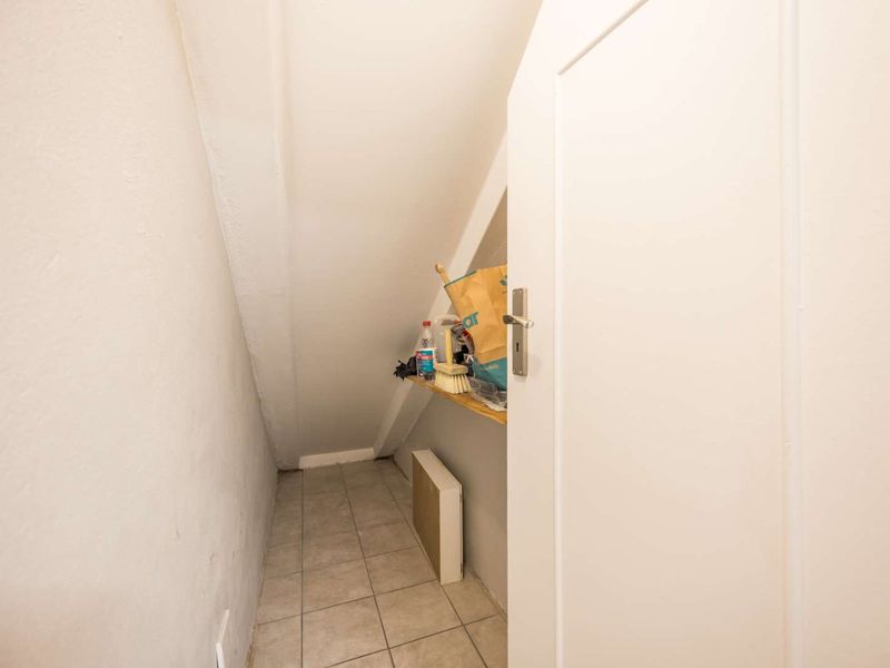 A compact under-stair utility storage space featuring tiled flooring and built-in shelving.