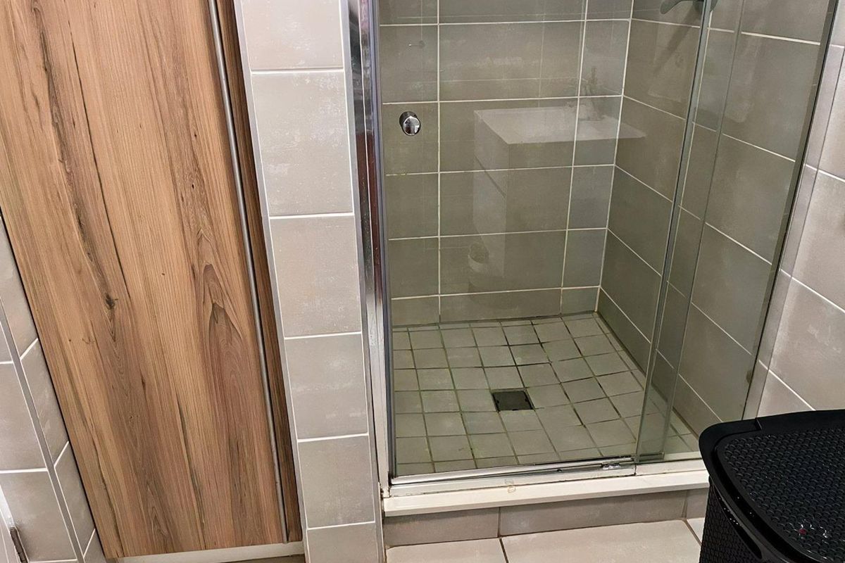 A bathroom shower enclosure featuring glass doors, neutral wall tiling, and wood-look cabinetry.