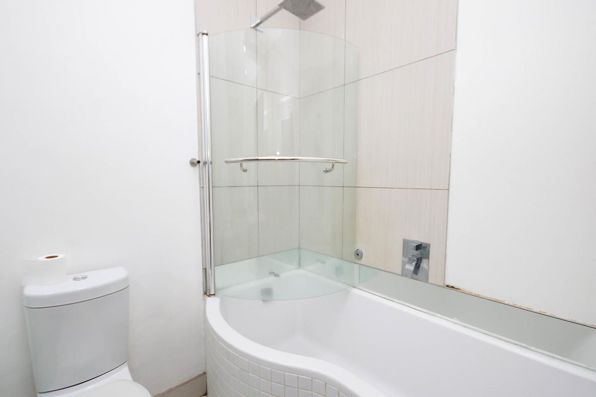A clean bathroom featuring a curved bathtub with a glass shower screen, wall-mounted shower head, and modern tiled wall finishes.