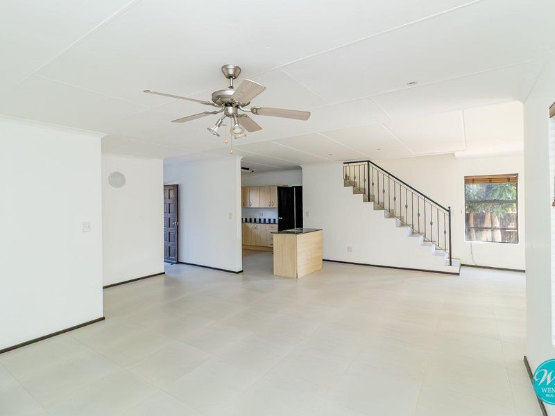 Spacious open-plan living area featuring tiled floors, a ceiling fan, and a staircase, with a view into the adjacent kitchen area.