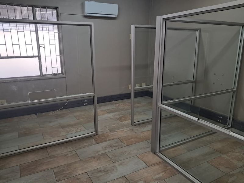 An office space featuring glass partition walls, tiled flooring, and a wall-mounted air conditioning unit.