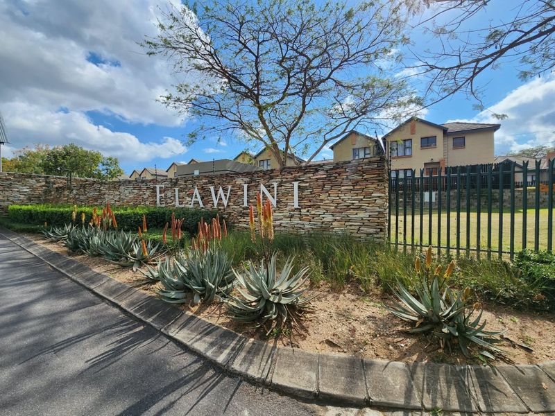 The entrance to Elawini estate featuring a decorative stone boundary wall, metal security fencing, and well-maintained landscaped garden beds.