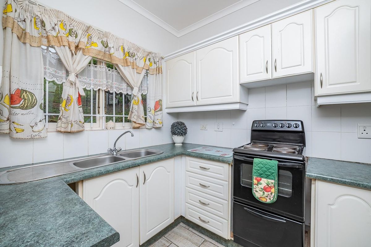 A functional kitchen featuring white cabinetry, laminate countertops, a double bowl stainless steel sink, and a freestanding electric stove with a tiled backsplash.