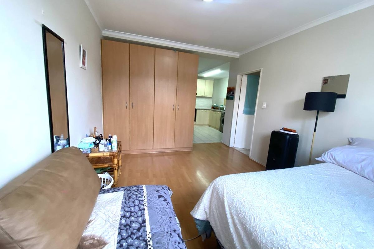 A bedroom featuring laminate flooring, a large built-in wardrobe, and direct access to the kitchen area.