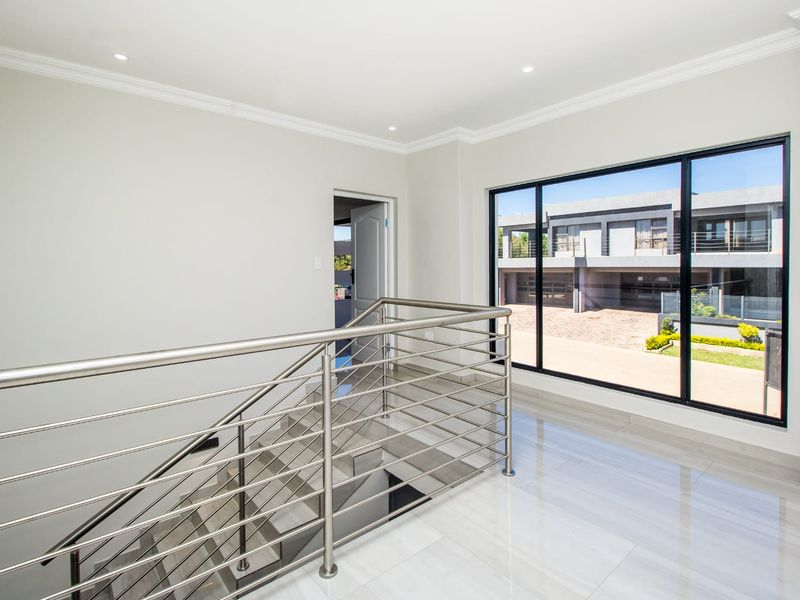 Bright and modern upper-level landing featuring polished tiled flooring, a sleek stainless steel balustrade, and large windows overlooking the estate.