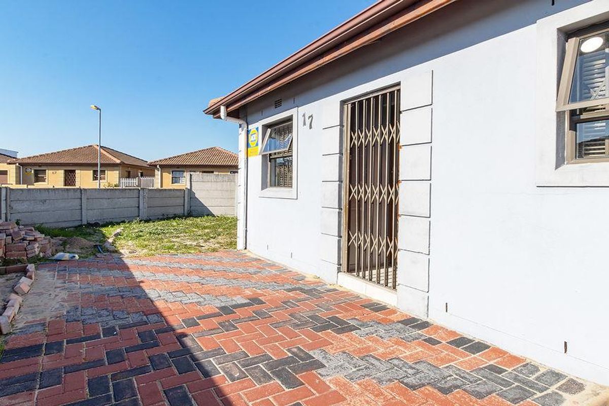Rear exterior view featuring a paved patio area, security gate, and precast concrete boundary wall in a residential setting.