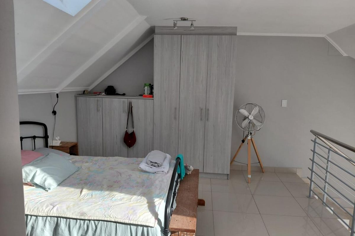 Loft-style bedroom featuring built-in cupboards, tiled flooring, a skylight, and a metal balustrade overlooking the lower level.