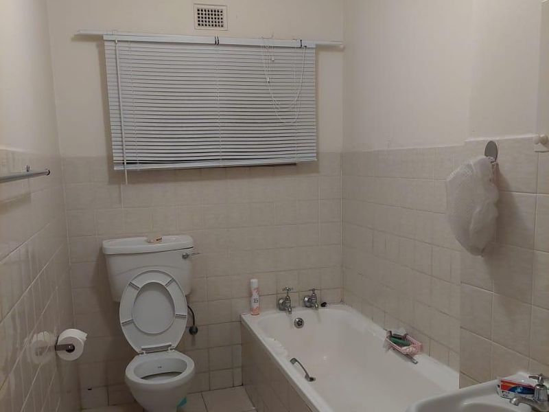 A dated bathroom featuring a standard bathtub, pedestal basin, and toilet with tiled finishes throughout.