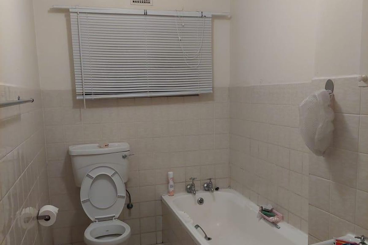 A dated bathroom featuring a standard bathtub, pedestal basin, and toilet with tiled finishes throughout.