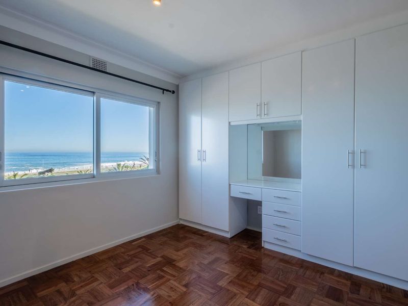 Bright bedroom featuring classic parquet flooring, extensive built-in cabinetry with an integrated vanity, and large windows offering scenic ocean views.