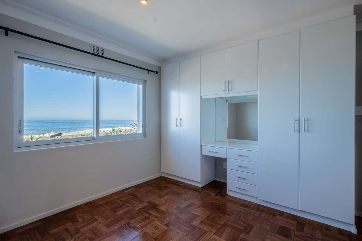 Bright bedroom featuring classic parquet flooring, extensive built-in cabinetry with an integrated vanity, and large windows offering scenic ocean views.