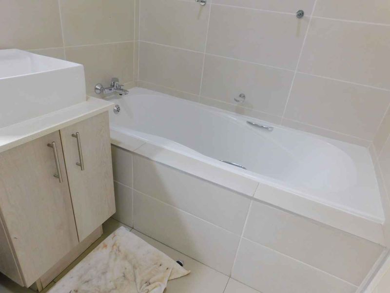 A clean, neutral-toned bathroom featuring a built-in vanity with a basin and a standard bathtub with tiled surround.