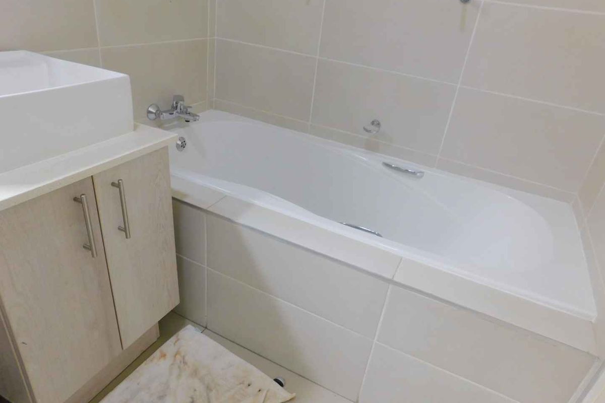 A clean, neutral-toned bathroom featuring a built-in vanity with a basin and a standard bathtub with tiled surround.