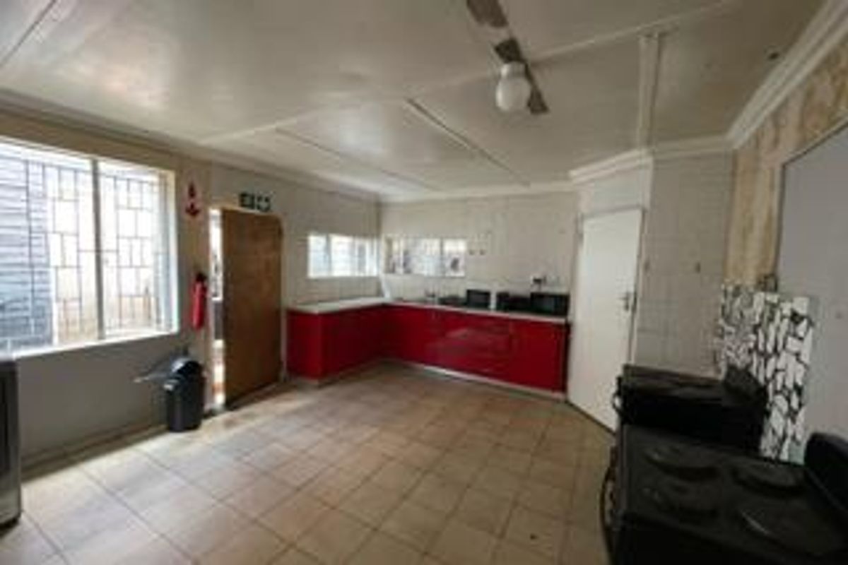 A spacious kitchen featuring red cabinetry, tiled flooring, and security bars on windows, offering a functional layout in need of cosmetic updates.