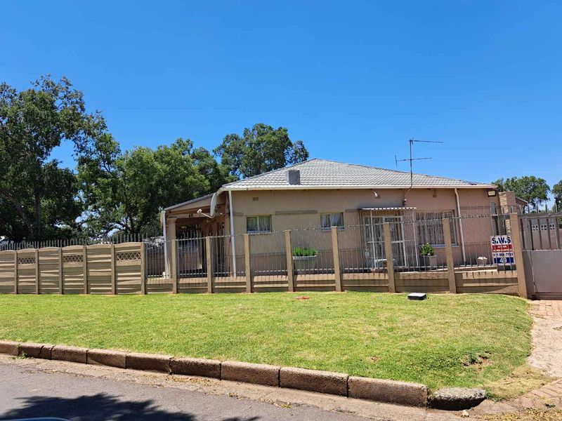 Front view of a single-story residential house featuring a tiled roof, security fencing, and a gated entrance.