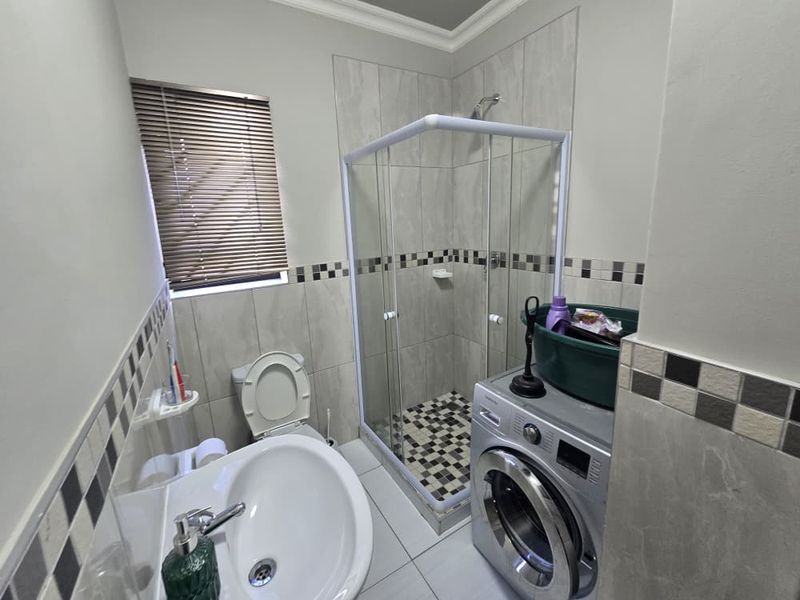 A functional bathroom featuring a shower enclosure, pedestal basin, and toilet, finished with neutral wall tiles and a decorative mosaic border.