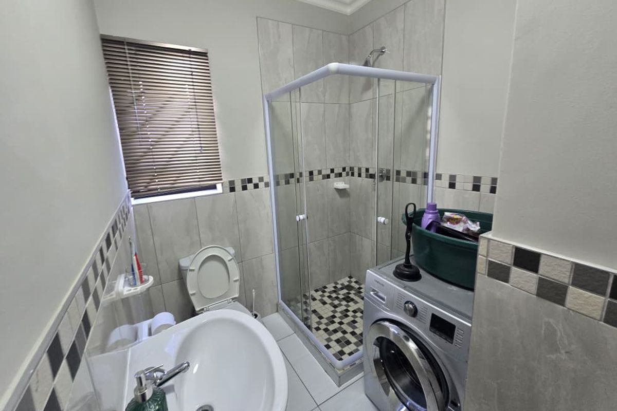A functional bathroom featuring a shower enclosure, pedestal basin, and toilet, finished with neutral wall tiles and a decorative mosaic border.
