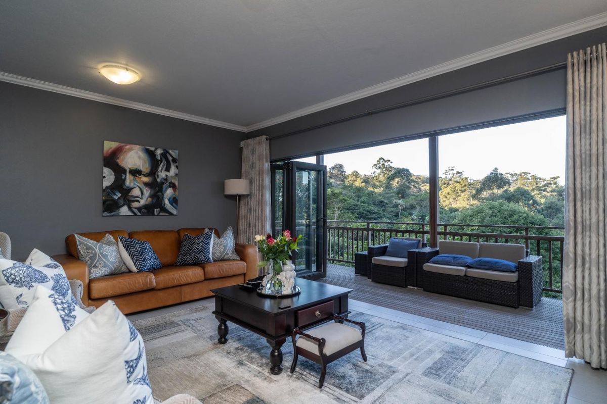 Spacious living room featuring large sliding glass doors that open onto a balcony with scenic forest views, complemented by neutral tiled flooring.