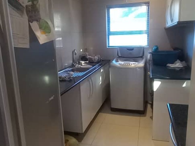 A functional scullery featuring built-in cabinetry, granite countertops, a stainless steel sink, and tiled flooring, providing additional workspace and utility storage.
