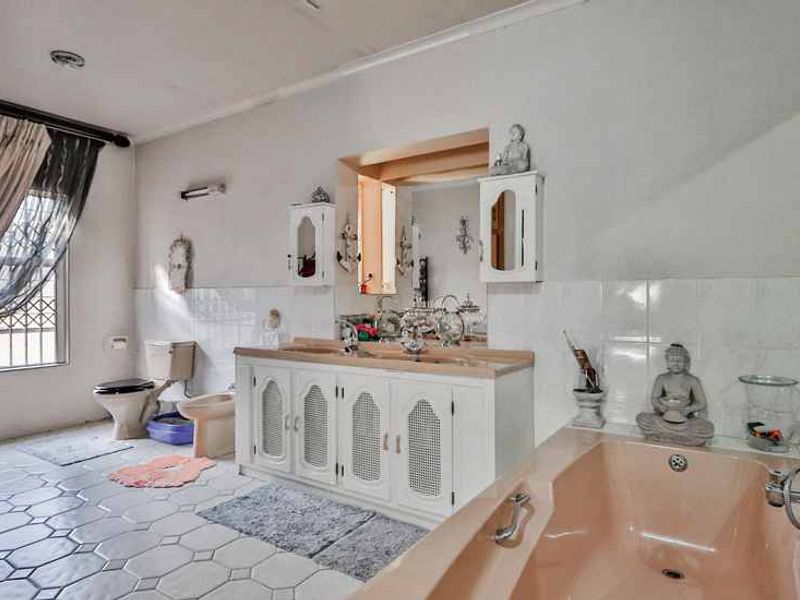 Spacious bathroom featuring a double vanity, built-in bathtub, toilet, and bidet, with tiled flooring and security bars on the window.
