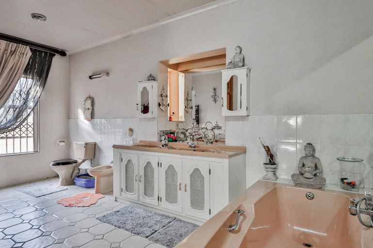 Spacious bathroom featuring a double vanity, built-in bathtub, toilet, and bidet, with tiled flooring and security bars on the window.