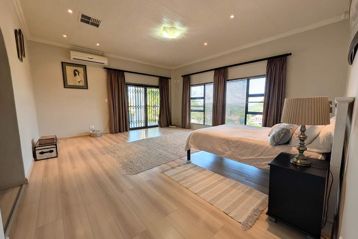 Spacious bedroom featuring light laminate flooring, recessed downlighting, a split-system air conditioner, and large windows with access to an outdoor area.