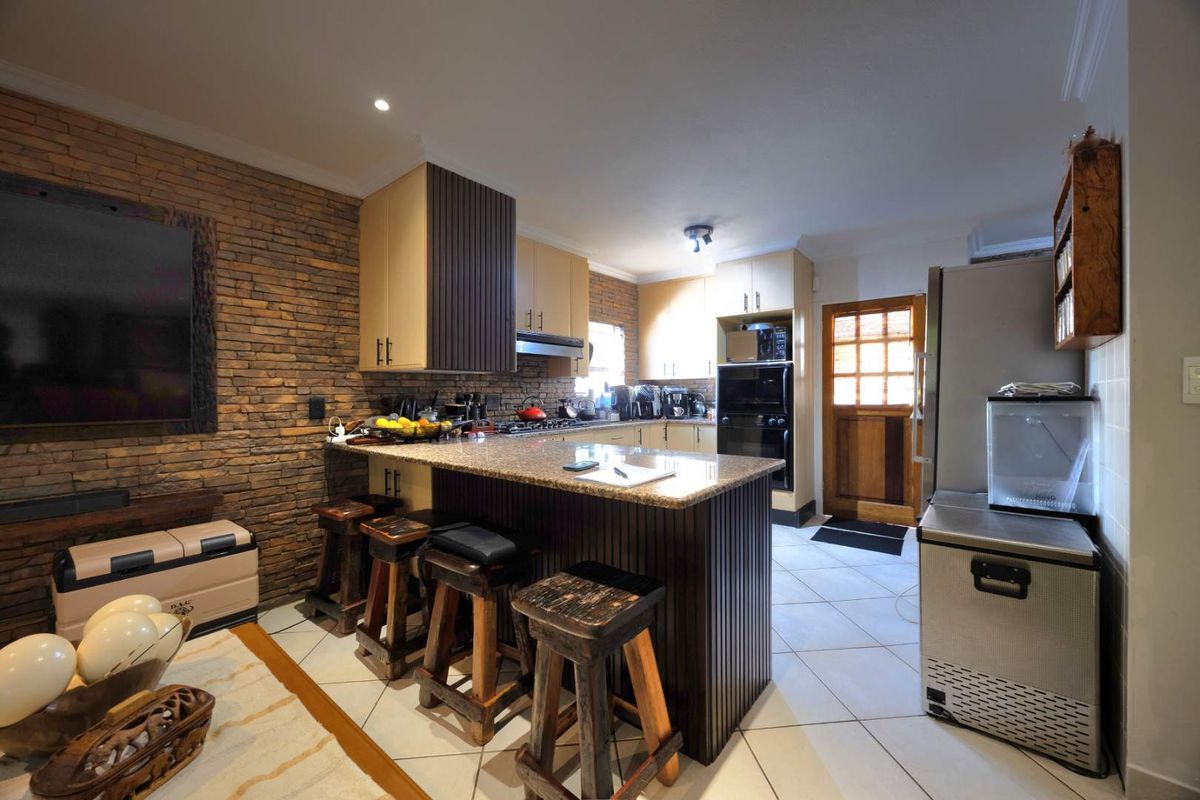 A functional kitchen featuring granite countertops, built-in appliances, an exposed brick feature wall, and tiled flooring with direct access to the exterior.
