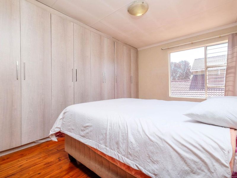 A bedroom featuring light-toned built-in cupboards, warm wooden flooring, and a window providing natural light.