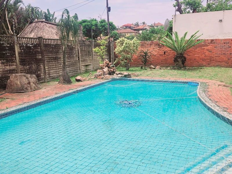 Outdoor swimming pool area featuring brick paving, a brick boundary wall, and precast concrete fencing in a residential garden setting.
