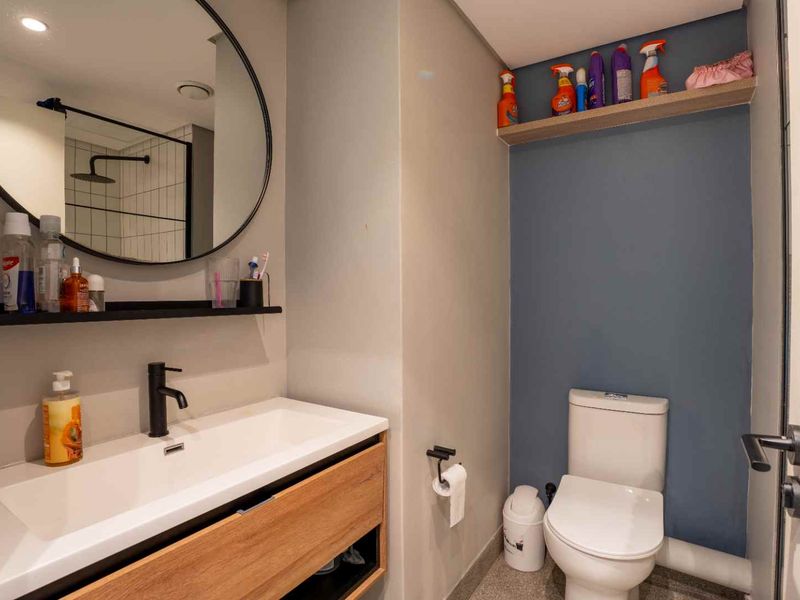 Modern bathroom featuring a wood-finish vanity with a white basin, black faucet, circular mirror, and a wall-mounted toilet.