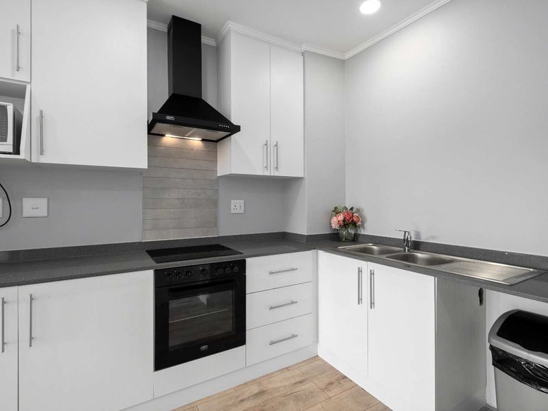 Modern kitchen featuring white cabinetry, dark stone countertops, integrated electric oven, hob, extractor fan, and a double bowl sink with laminate flooring.