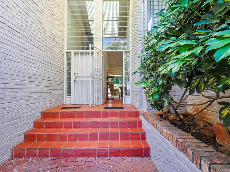 Front entrance of the townhouse featuring a brick facade, tiled steps, and a secure metal gate leading into the home.