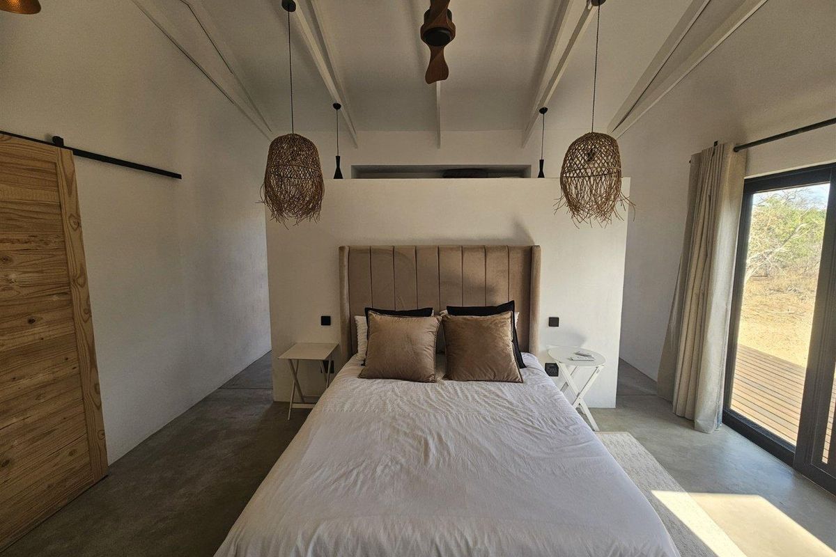 A modern bedroom featuring polished concrete floors, a vaulted ceiling with exposed beams, and a sliding barn door, with direct access to an outdoor deck.