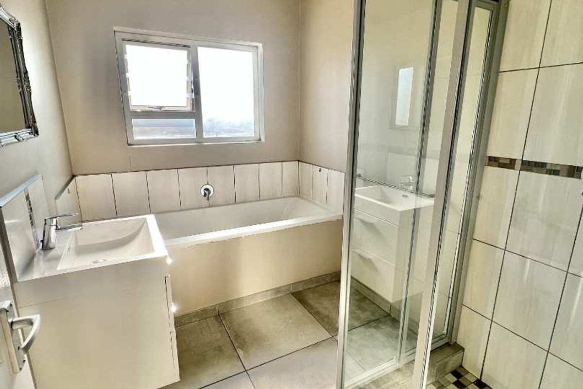 Modern bathroom featuring a white vanity, a built-in bathtub, and a separate glass-enclosed shower with tiled flooring.