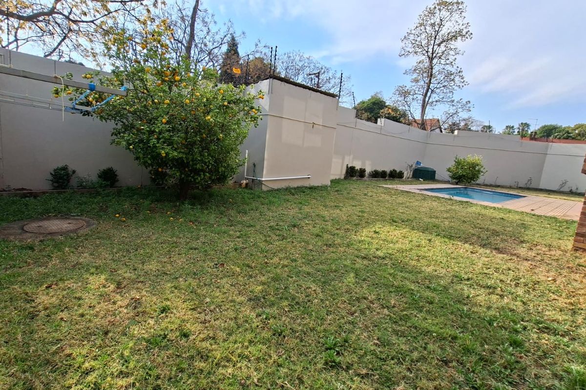 A private rear garden featuring a swimming pool, established lawn, and high perimeter walls with electric fencing for added security.