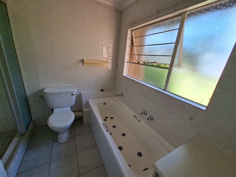 A dated bathroom featuring a bathtub, separate shower enclosure, and toilet, with tiled walls and flooring throughout.